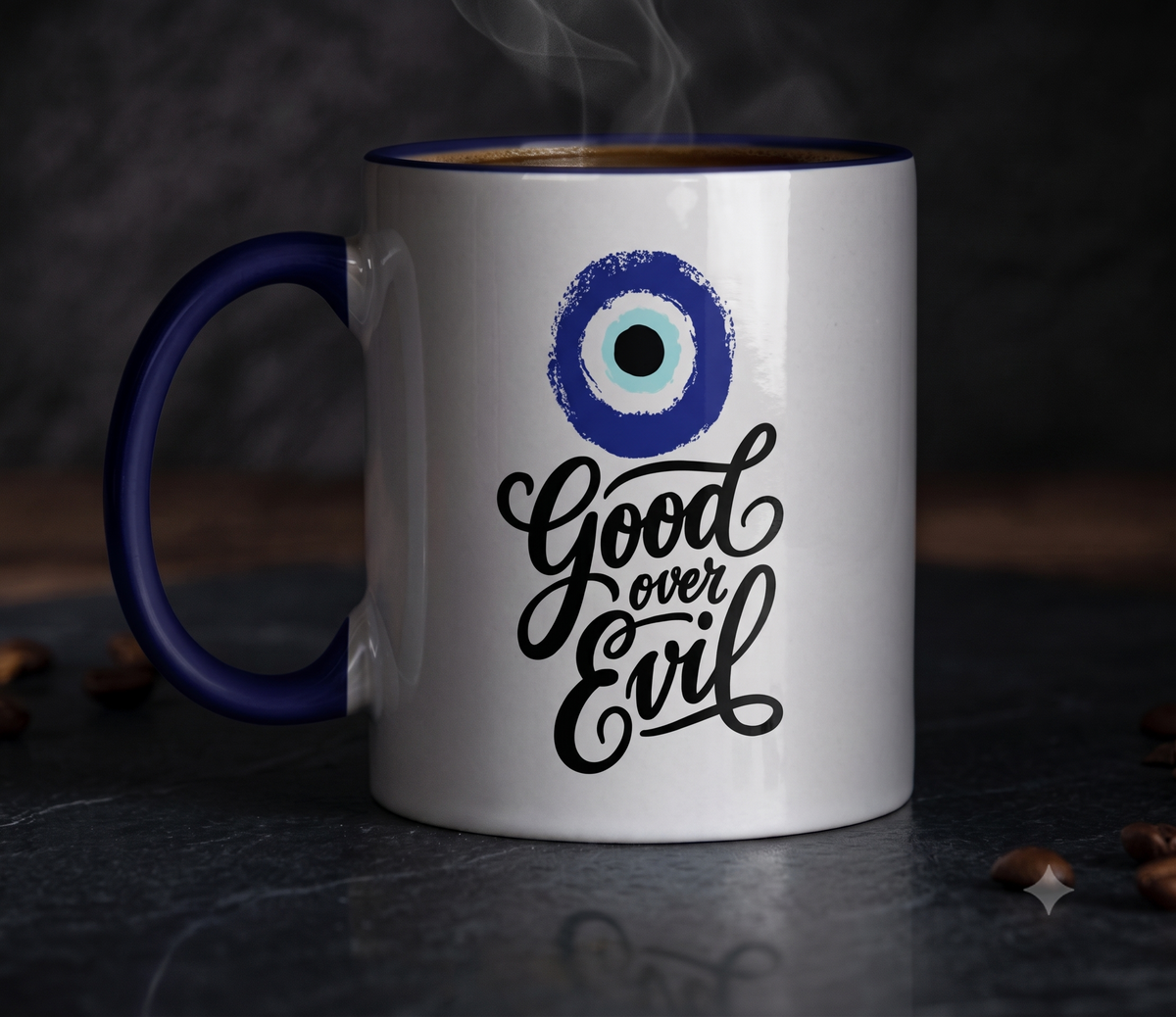 A white ceramic coffee mug with a dark blue handle and rim, featuring a blue and white evil eye graphic and the phrase 'Good over Evil' in black script. Steam rises from the top, and coffee beans are scattered on a dark, moody surface.