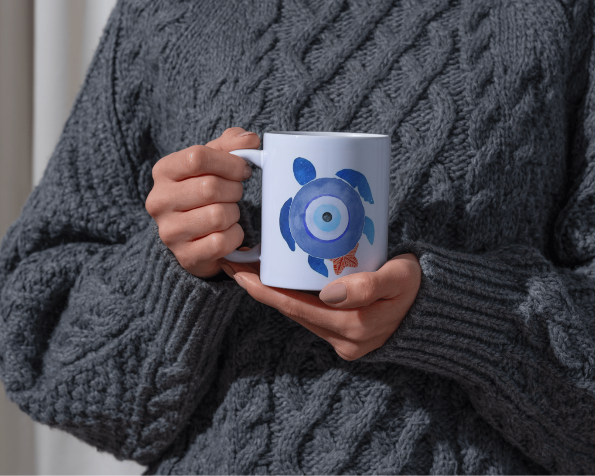 Person wearing a gray sweater holding a white mug with a blue design.